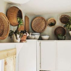 baskets and plants sit on top of a cabinet in a room with white cupboards