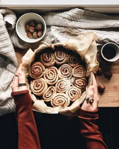 a person holding a pan filled with cinnamon rolls on top of a wooden cutting board