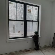 a young boy standing in front of a window looking out at the snow covered ground