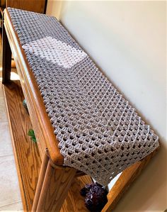 a crocheted table runner sitting on top of a wooden bench next to a wall