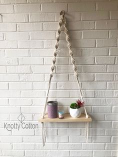 a white brick wall with a shelf holding two cups and a potted plant on it