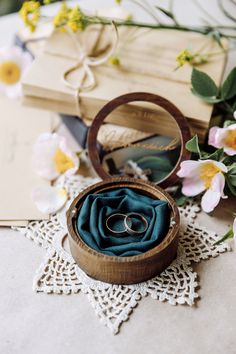 two wedding rings in a wooden box on a lace doily next to some flowers