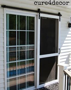 an open sliding glass door on the side of a white house with black shutters