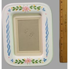 a white and blue frame with flowers on it next to a ruler that is measuring