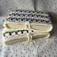 three crocheted books sitting on top of a bed covered in white and pink flowers