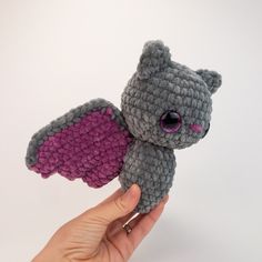 a hand holding a small gray and purple stuffed animal with pink wings on it's back