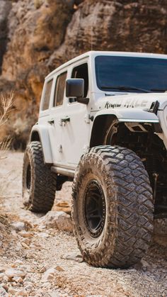 a white jeep is parked on the side of a rocky road in front of a mountain