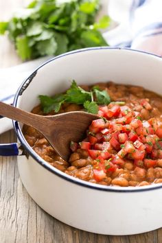 a white pot filled with beans and garnish on top of a wooden table