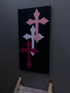 an easel is sitting in front of a painting with pink and white crosses on it