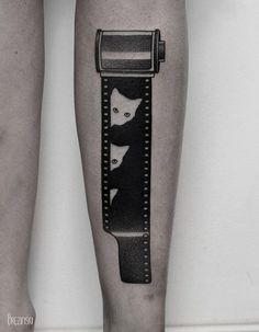 black and white cat tattoo on the leg of a woman's legs, with an image of two cats in a tube attached to it