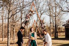 a man and woman standing next to each other in front of a wooden arch with flowers on it