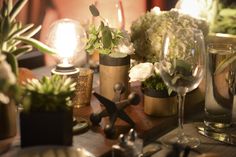 a table topped with lots of different types of vases and plants next to wine glasses