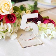 the number five is surrounded by flowers and greenery on top of a table cloth