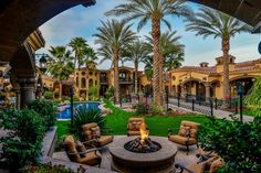 an outdoor fire pit surrounded by palm trees and lawn furniture with a pool in the background