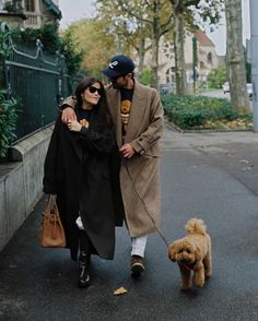 a man and woman are walking their dog down the street while wearing winter clothes,