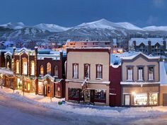 a small town is covered in snow and lit up at night with mountains in the background