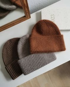 three knit beanies sitting on top of a white table next to a framed mirror