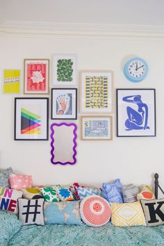 a couch covered in lots of different types of pillows and pictures on the wall above it