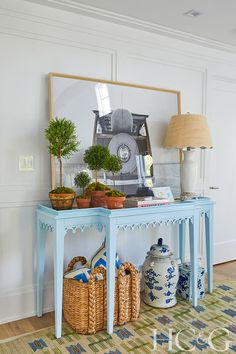 a blue table topped with potted plants next to a lamp and pictures on the wall