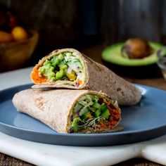 a burrito on a blue plate with avocado and other fruit in the background