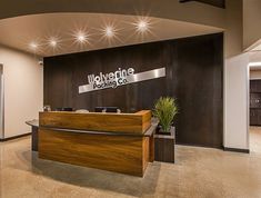 an office lobby with a reception desk and lights on the ceiling, along with two planters filled with potted plants