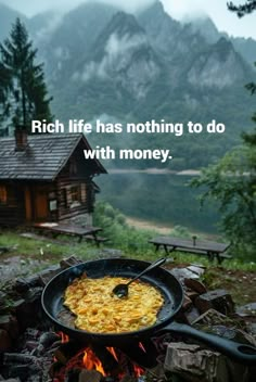 a skillet filled with food sitting on top of a fire pit in front of a cabin