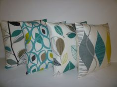 four decorative pillows are lined up on a white surface, one is green and the other is blue