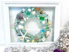 a wreath made out of sea glass and seashells is displayed in a white frame