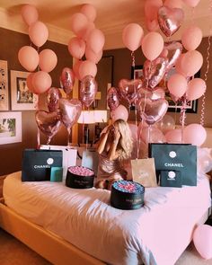 a woman sitting on top of a bed with pink and gold balloons hanging from the ceiling