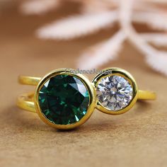 two gold rings with green and white diamonds on top of each other, sitting on a brown surface