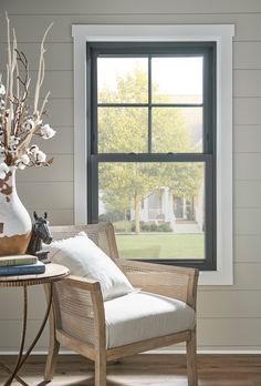 a chair and table in front of a window with a vase filled with flowers on it