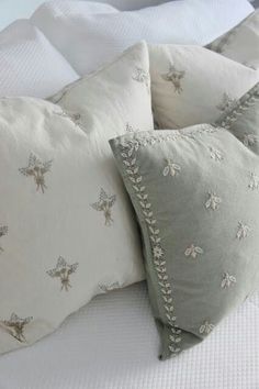 two pillows on top of a bed with white linens and silver embroidered bee designs