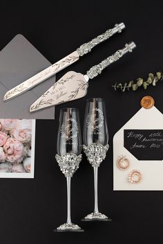 two champagne flutes with wedding decorations on the table next to an envelope and some cards