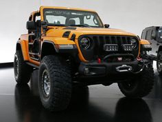 an orange jeep is parked next to another black jeep in a white walled room with dark floors