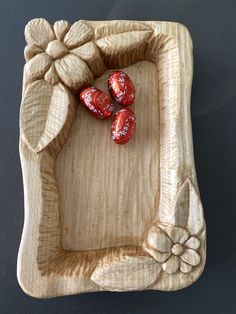 four chocolate candies in a carved wooden tray on a black surface with flowers and leaves