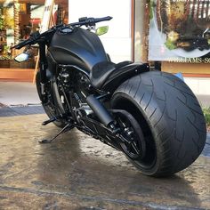 a black motorcycle parked on top of a sidewalk next to a store front window,