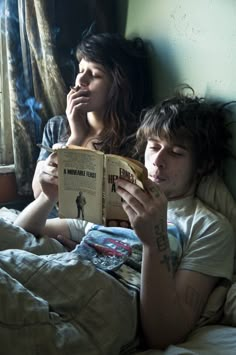 a man and woman laying in bed reading a book