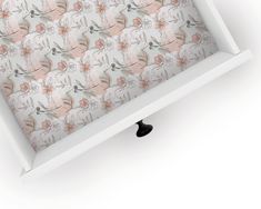 an open drawer with floral wallpaper on the bottom and handles in white painted wood