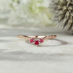 a gold ring with three red stones on the front and side, sitting next to a pine cone