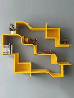 a yellow shelf with books on it against a gray wall next to a vase and other items