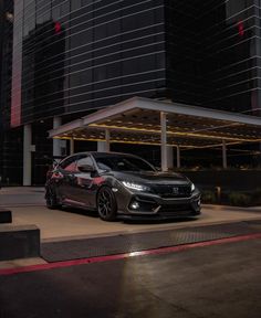 a black car parked in front of a tall building at night with its lights on