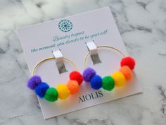 a pair of hoop earrings with multi colored pom - poms on top of it