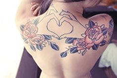 the back of a woman's body with tattoos on it and flowers around her neck