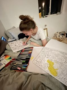 a woman laying on top of a bed with lots of coloring books