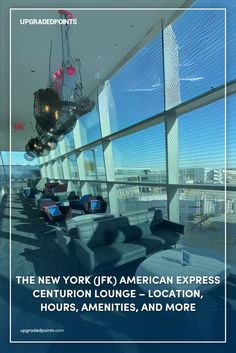 Interior of the New York (JFK) American Express Centurion Lounge, featuring modern seating arrangements with blue and purple chairs, large floor-to-ceiling windows overlooking the airport runway, and contemporary black pendant lighting hanging from the ceiling.