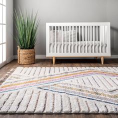 a white crib with a rug and potted plant next to it on the floor