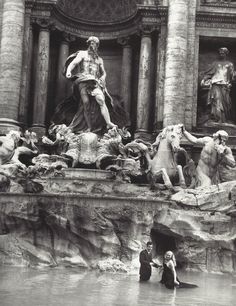 an old black and white photo of people standing in front of a fountain with statues