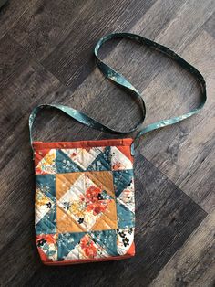 an orange and blue patchwork bag sitting on top of a wooden floor next to a green strap