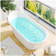 a bathtub with blue water in it on a wooden floor next to a window