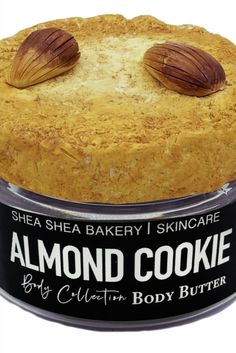 a cake in a tin with two almonds on top that says almond cookie by ellen's body butter